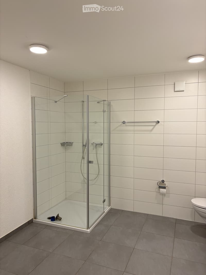 empty shower room with toilet, glass wall, white tiles, white toilet