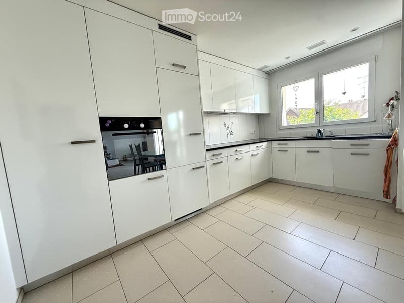 Modern kitchen with white cabinets, tiled floor, and large windows. Features a sink, faucet, and built-in oven.