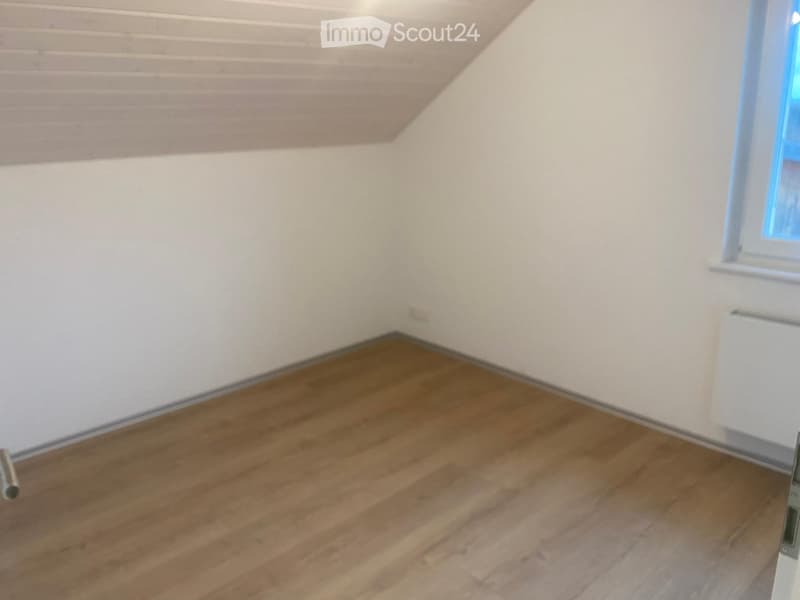 Empty room with wooden flooring and white walls, featuring a window and radiator on one side.