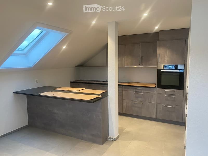 Modern kitchen with grey cabinets, a central island, and a built-in oven. Features a skylight window and recessed lighting.