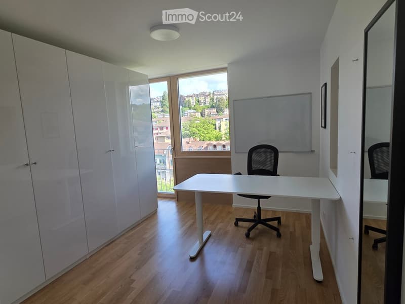 Modern office space with a white desk, ergonomic chair, large wardrobe, and a large window offering a view of the city.