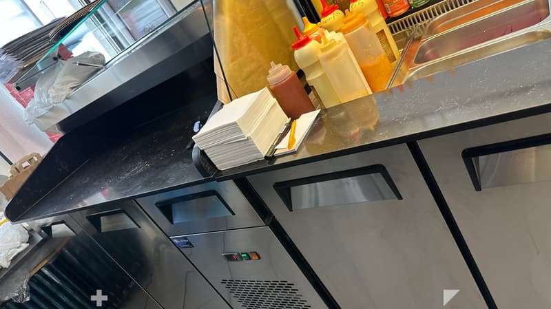 Commercial kitchen counter with condiments, napkins, and a stainless steel appliance.