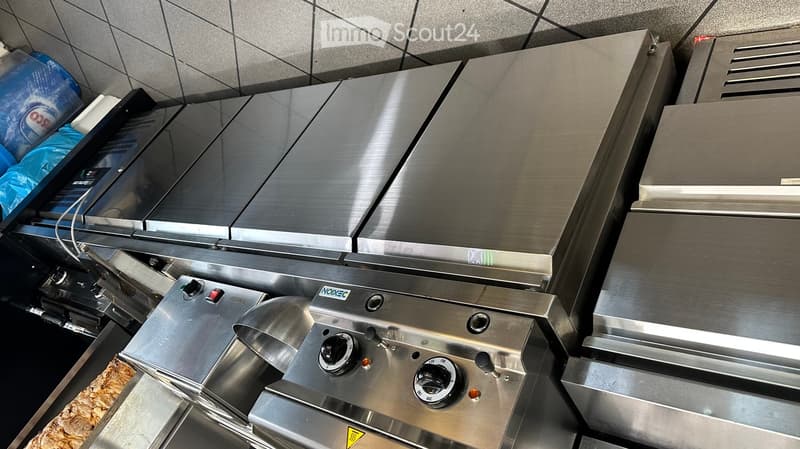 Stainless steel commercial kitchen stove with multiple burners and control knobs, featuring a vent hood above.