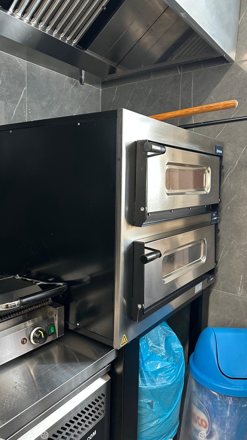 Commercial kitchen with stainless steel ovens, grill, and trash bins.