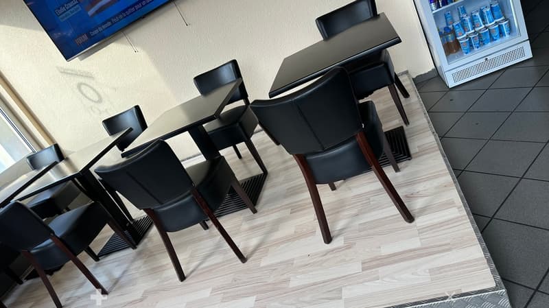 Modern dining area with black leather chairs, glass tables, and a small refrigerator stocked with drinks.