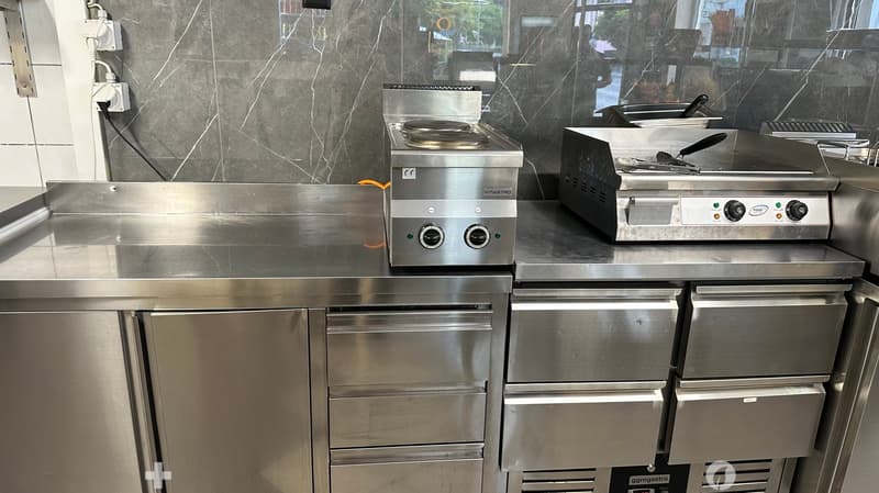 Commercial kitchen with stainless steel surfaces, induction hob, fryer, and refrigerator.