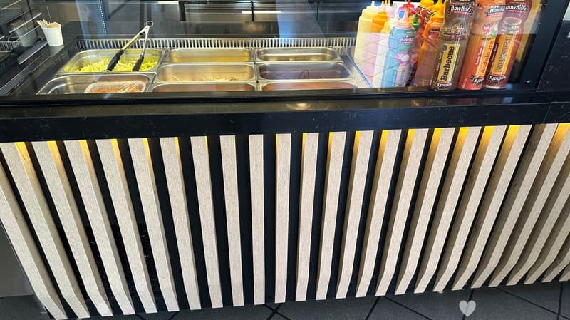 Food display counter with stainless steel serving trays, tongs, and various condiments including sauces and dressings.