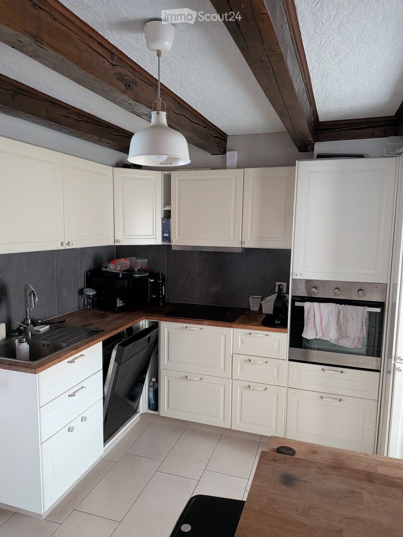 Modern kitchen with white cabinets, wooden countertops, stainless steel appliances, and a pendant light fixture.