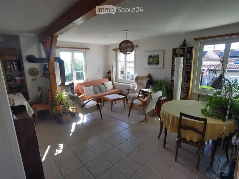 Bright living room with a tiled floor, large windows, a fireplace, a sofa, coffee table, chairs, a dining table, and bookshelves.