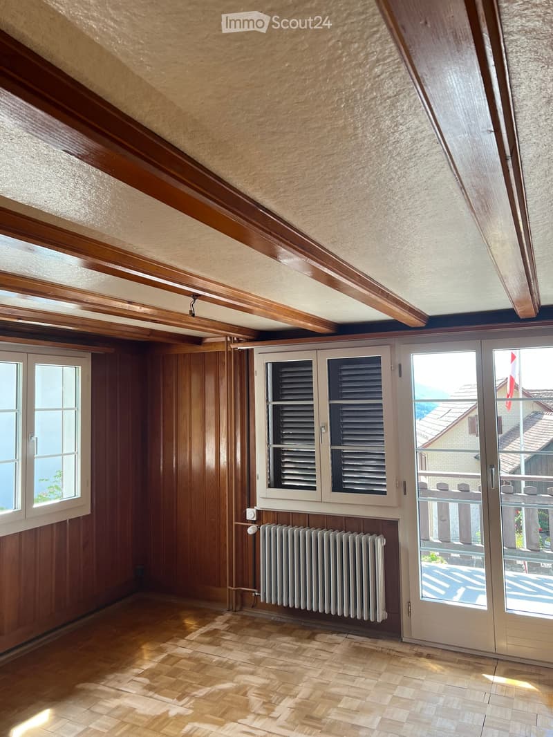 Empty attic room with wooden walls, wooden floor, large windows, radiator, and a door leading to a balcony.
