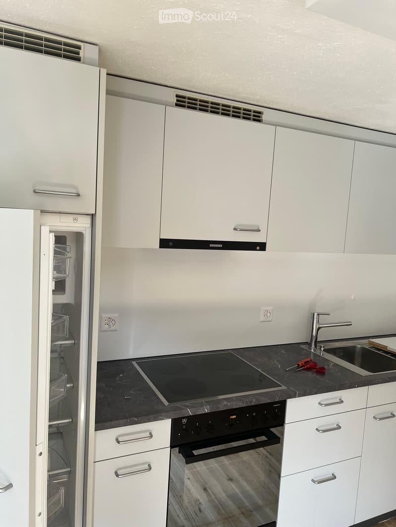 Modern kitchen with white cabinets, black countertops, stainless steel sink, induction cooktop, and built-in oven. The refrigerator is open, revealing shelves inside.