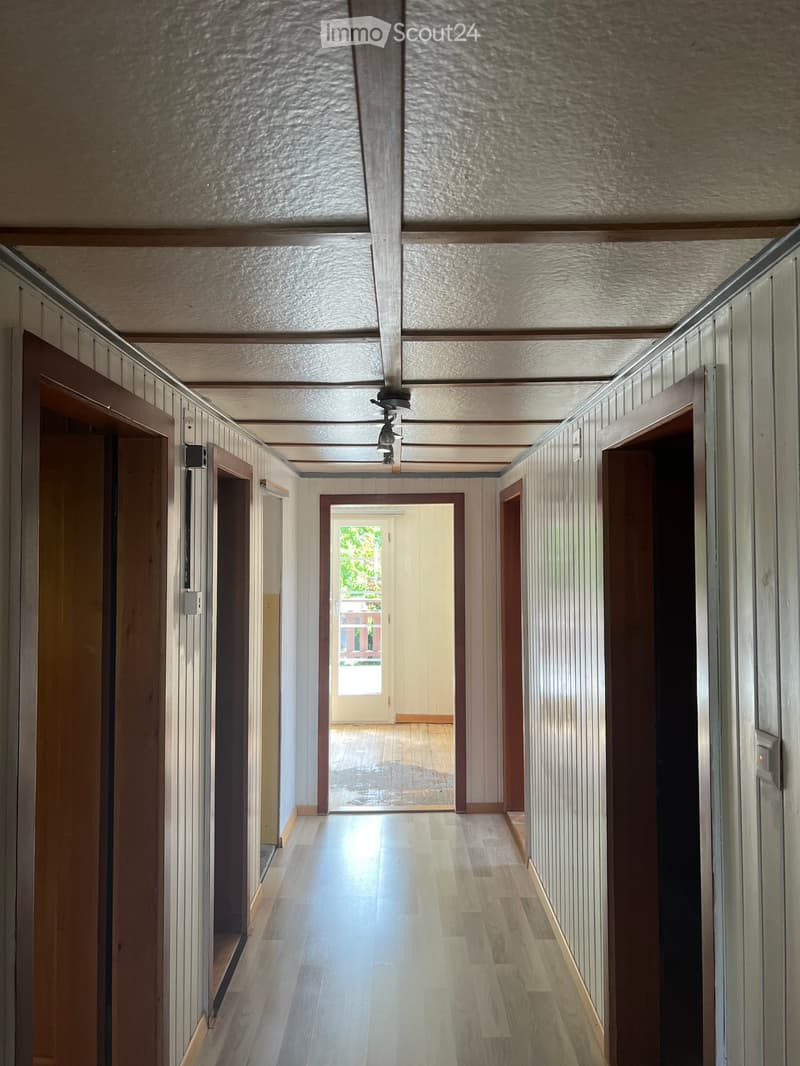 Wooden-paneled hallway with multiple doors, wooden flooring, and a ceiling light fixture.
