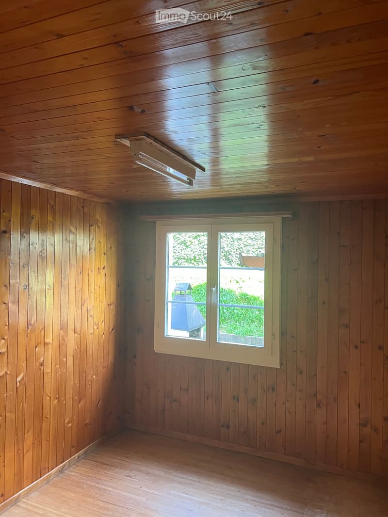 Empty room with wooden walls and ceiling, a single window with white frame, and a built-in light fixture on the ceiling.