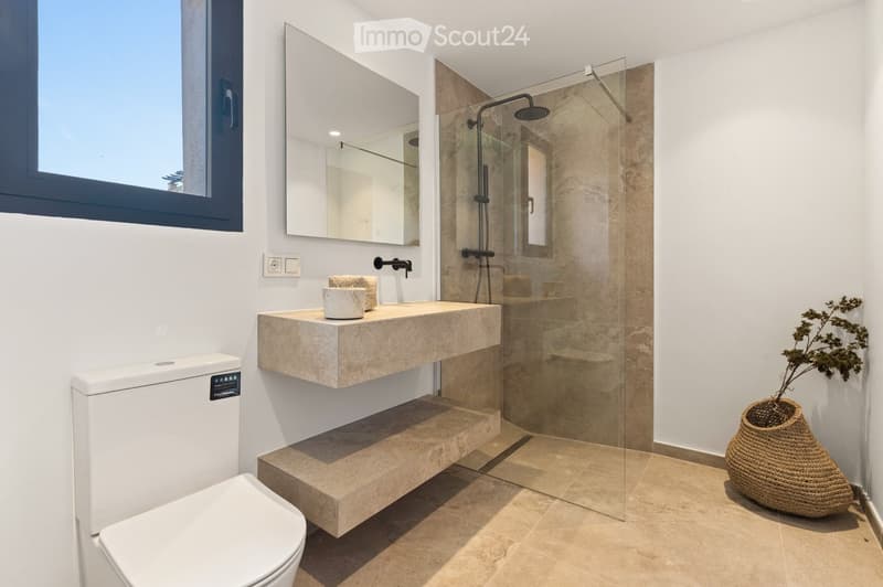 Modern bathroom with a floating sink, large mirror, glass-enclosed shower, and a decorative woven vase on the floor.