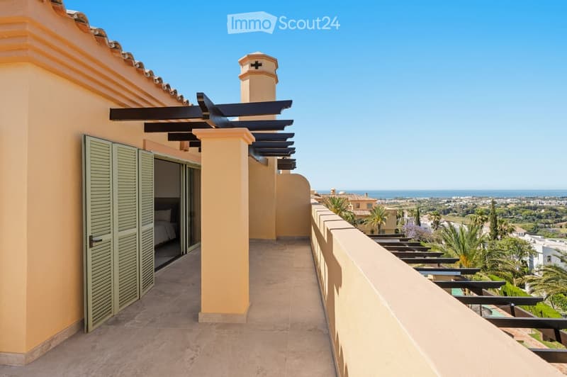 Spacious balcony with beige tiled flooring, wooden pergola, and a view of the sea and surrounding landscape.