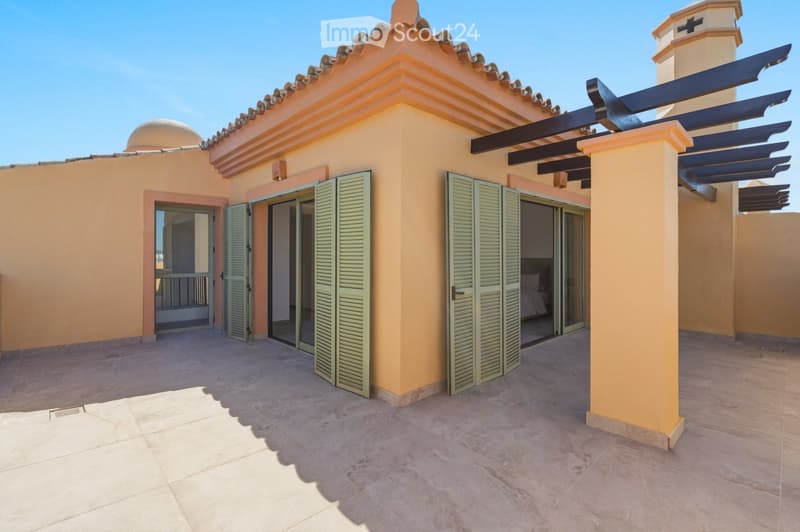 Balcony with tiled floor, green shutters, and a view of a bedroom with a bed inside. The balcony features a pergola with dark wooden slats and a small tower with a cross on top.