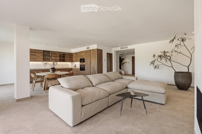 Modern living and dining area with a large sectional sofa, coffee table, dining table with chairs, and a kitchen area with wooden cabinets and appliances.