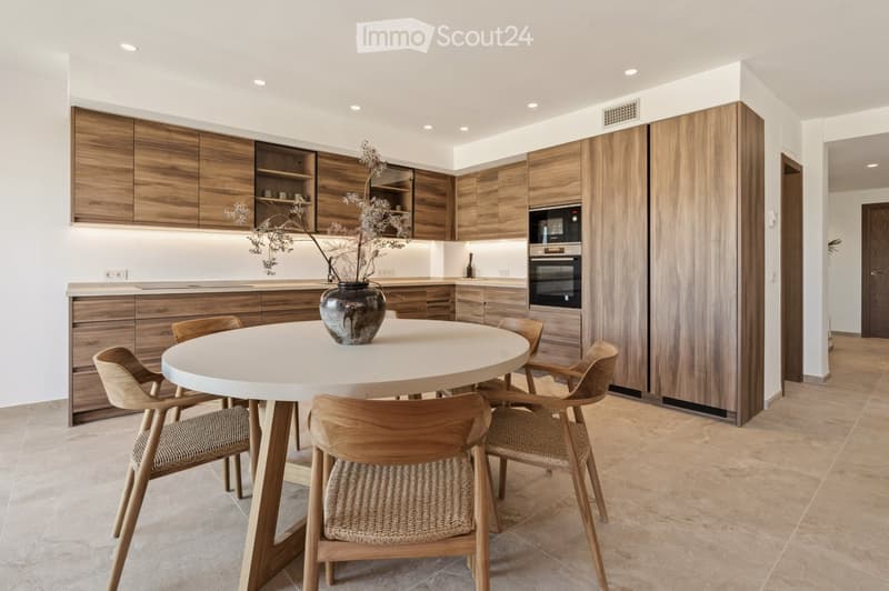 Modern kitchen with wooden cabinets, a round dining table with four chairs, and a vase with dried flowers on the table.
