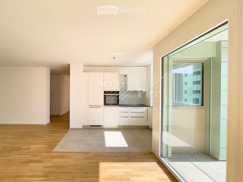 Modern kitchen with white cabinets, a built-in oven, and wooden flooring. Large window provides natural light.