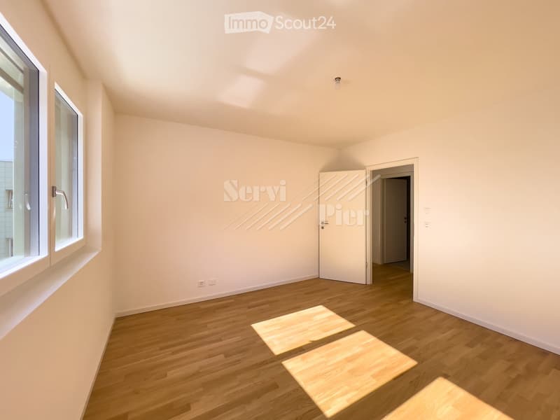 Empty room with wooden flooring, white walls, large windows, and a door leading to another space.