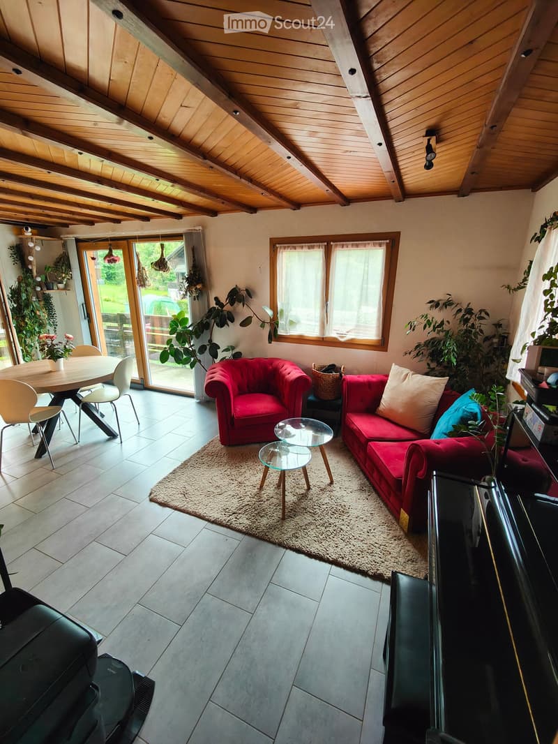 Living room with red sofa, glass coffee tables, dining table, and chairs, large windows, and plants.