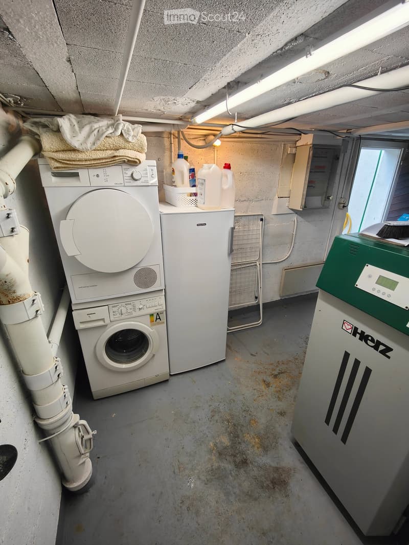 Utility room with a washing machine, dryer, refrigerator, towels, milk jugs, and an electrical panel.