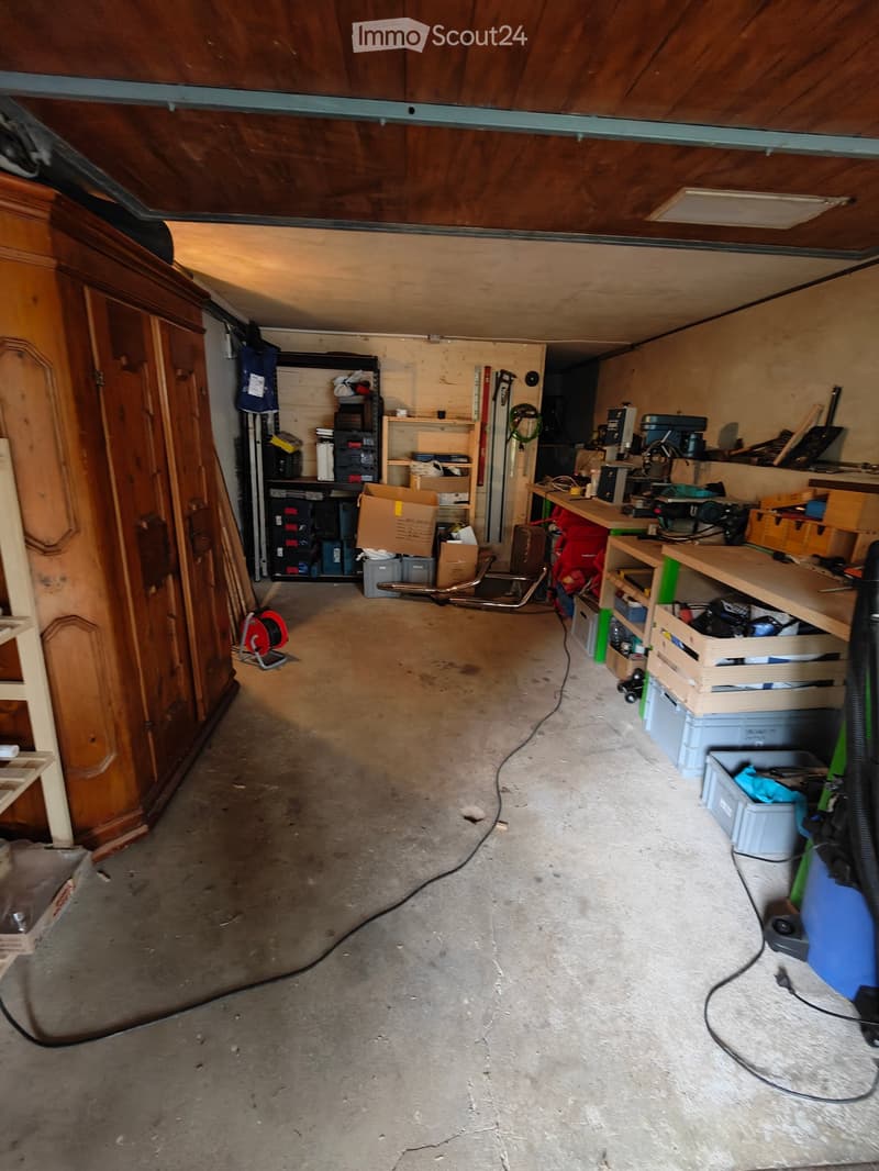 Empty garage with concrete floor, wooden ceiling, shelves, and storage items.