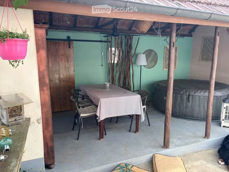 Outdoor patio area with a dining table, chairs, a hanging basket, a small lamp, and a hot tub.