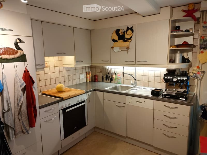 Modern kitchen with white cabinets, stainless steel appliances, and a double sink. Features include a refrigerator, oven, dishwasher, coffee maker, and a wooden cutting board with a fruit on it.