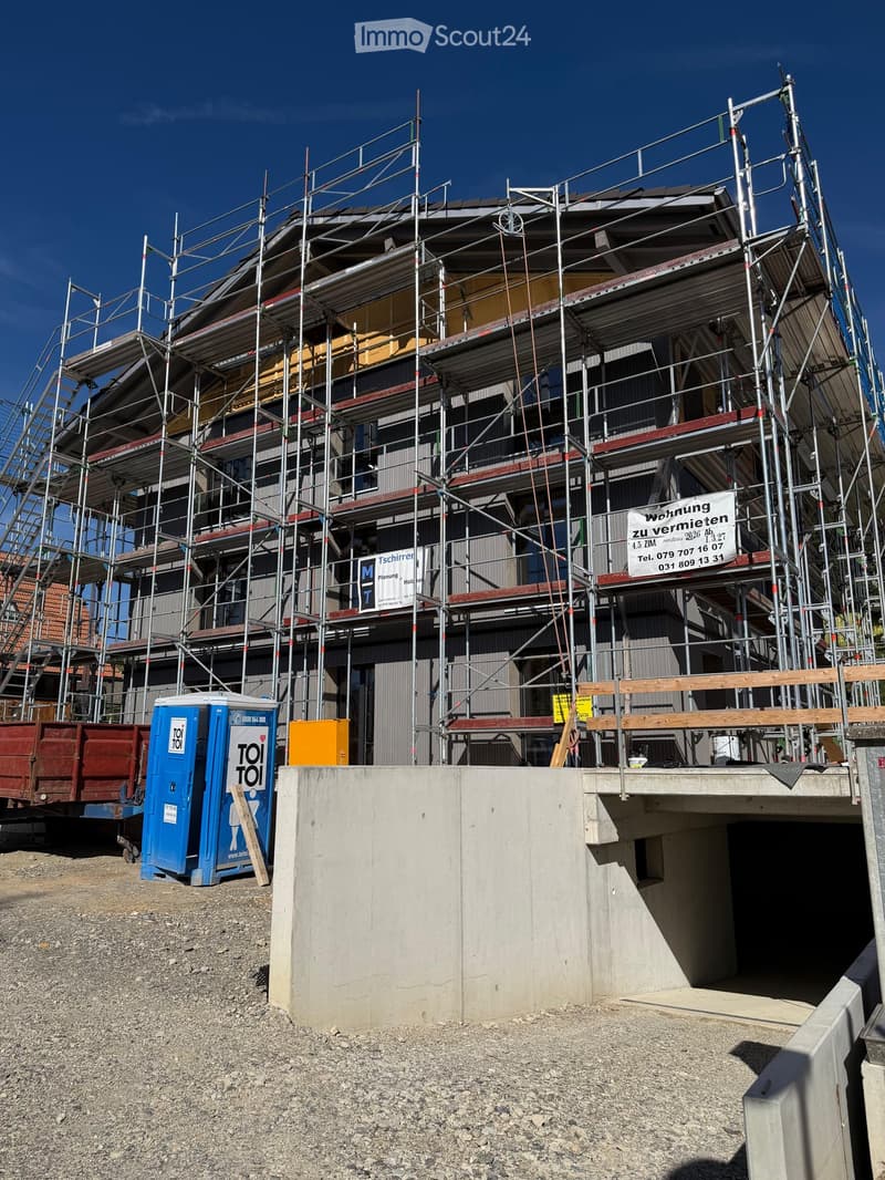 Multi-story building under construction with scaffolding, visible signage, and a portable toilet nearby.