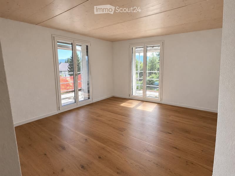 Empty room with wooden flooring, white walls, and large glass sliding doors leading to a balcony with a scenic view.
