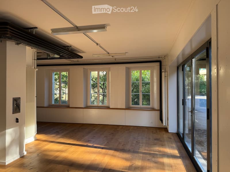 Empty room with wooden flooring, white walls, large windows, and a sliding glass door leading outside.
