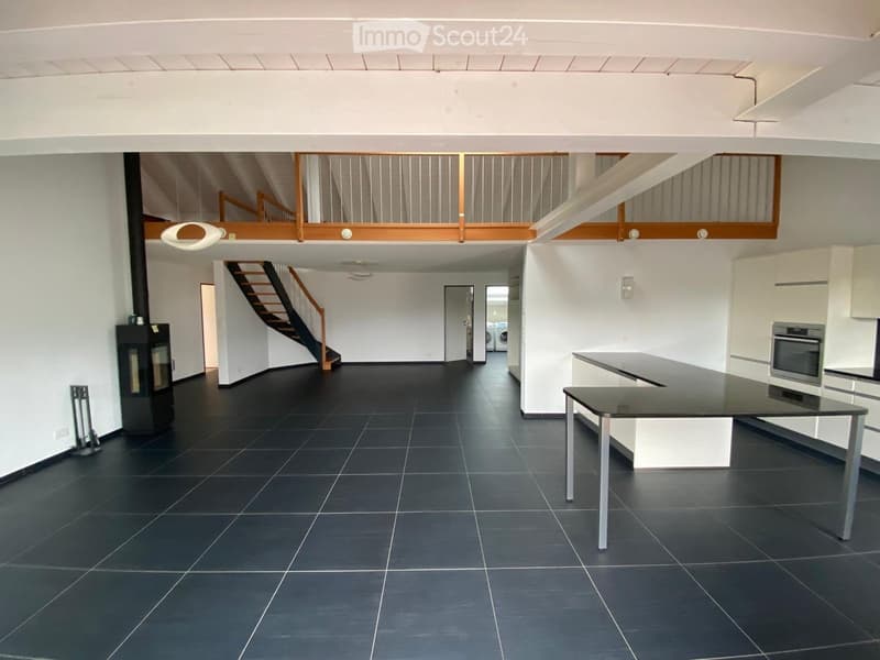 Open-plan space with dark tiled floor, white walls, staircase leading to an upper level, a fireplace, a kitchen area with a table and oven, and a modern design.