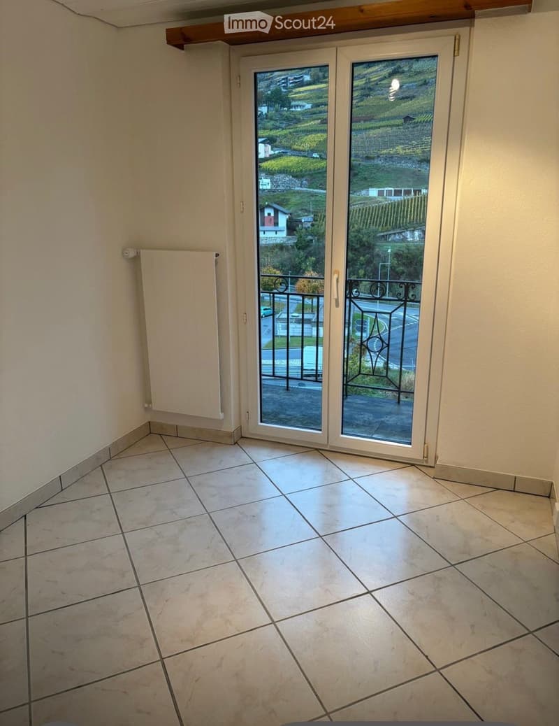 Empty room with tiled floor, white walls, and a sliding glass door leading to a balcony with a view of the countryside.