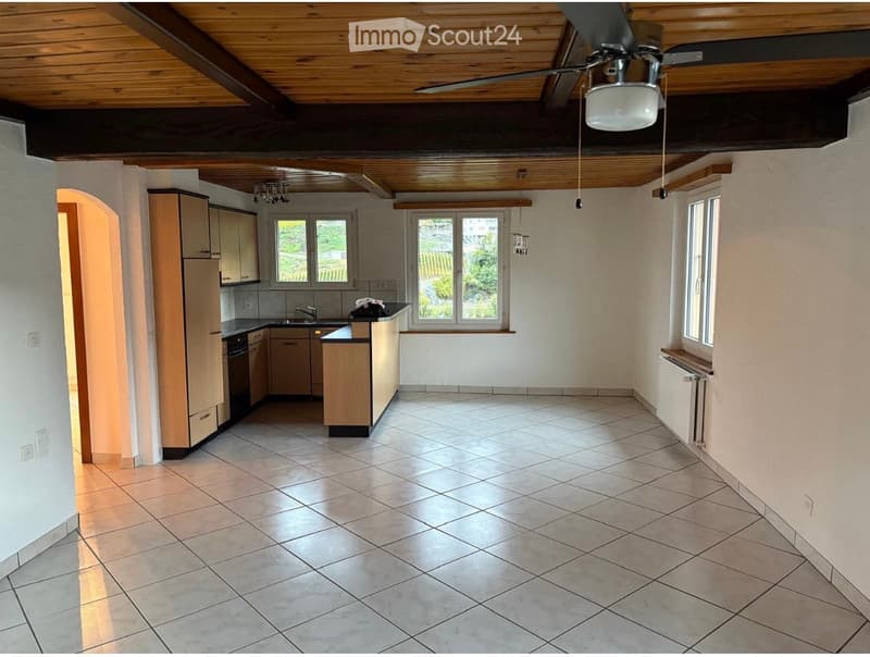 Bright kitchen with tiled floor, wooden cabinets, and a central island. Large windows provide natural light, and a ceiling fan with light fixture is visible.