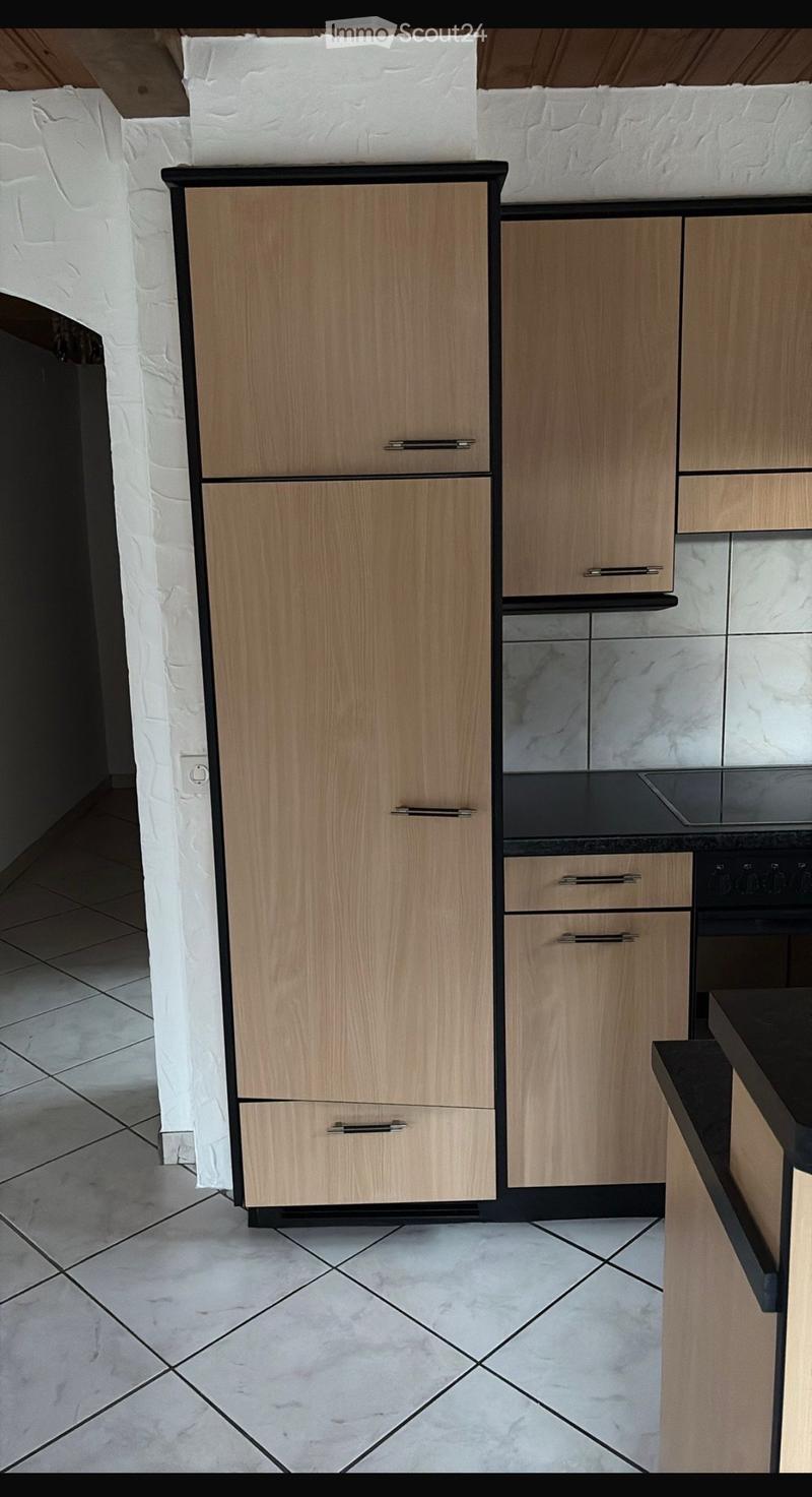 Modern kitchen with light wood cabinets, black handles, and marble countertops.