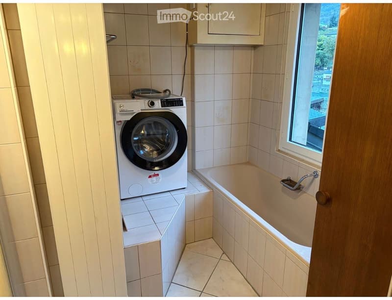 Bathroom with a bathtub, a washing machine, tiled walls, and a window offering a view.