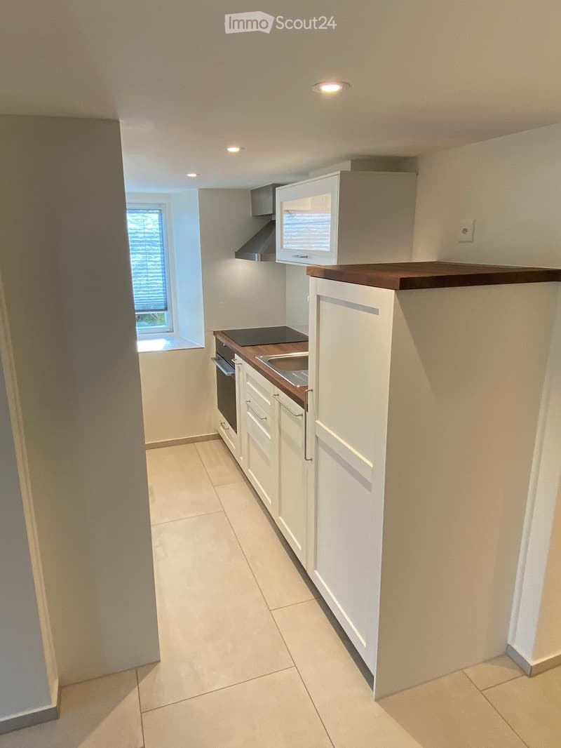 Modern kitchen with white cabinets, wooden countertops, and built-in appliances including a refrigerator, oven, and microwave. The space features tiled flooring and a window with blinds.