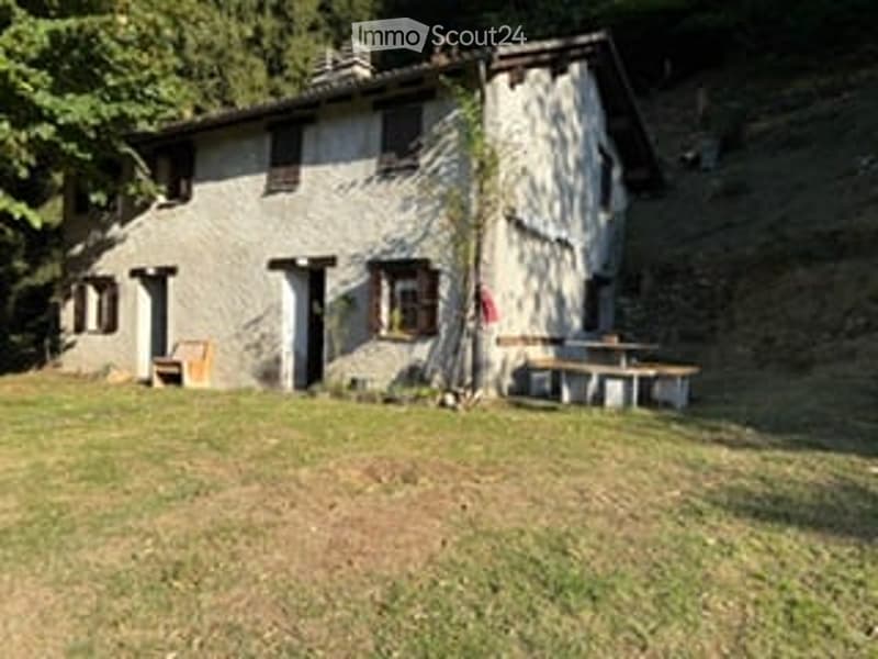 A rustic stone house with a small patio area featuring a table and chairs, surrounded by a grassy lawn.