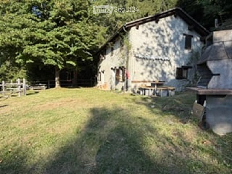 A rustic stone building surrounded by a grassy yard with trees and a wooden fence. There are outdoor seating areas and a stone staircase leading up to the building.