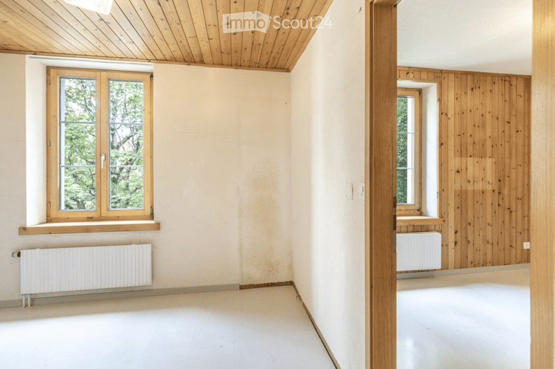 Empty room with wooden ceiling, white walls, large windows, and radiators. No furniture or equipment present.