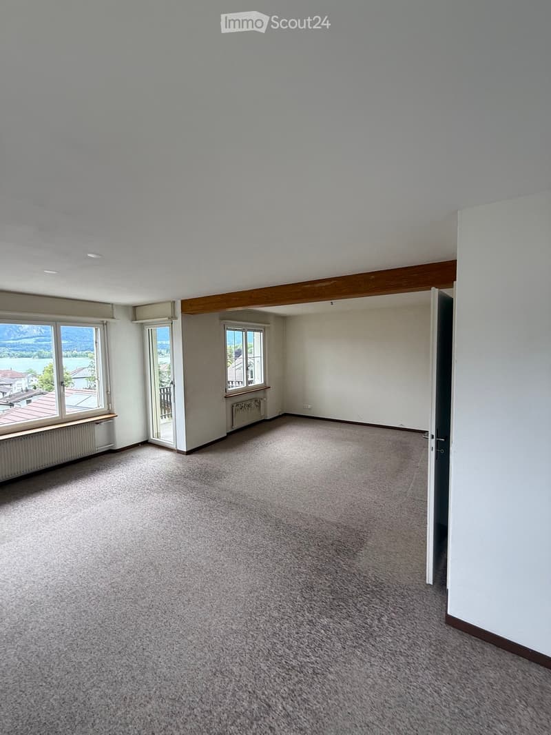 Empty room with carpeted floor, white walls, large windows, and a door leading to another space.
