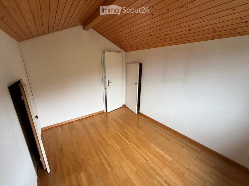 Empty room with wooden flooring, white walls, and a wooden ceiling. Two white doors are visible, one leading to another room.
