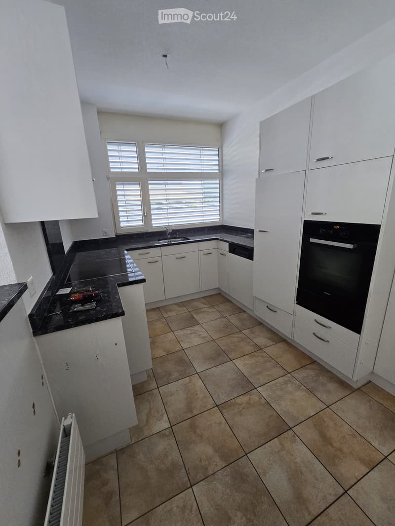 Modern kitchen with white cabinets, black countertops, and tiled flooring. Features include a sink, faucet, and built-in oven.