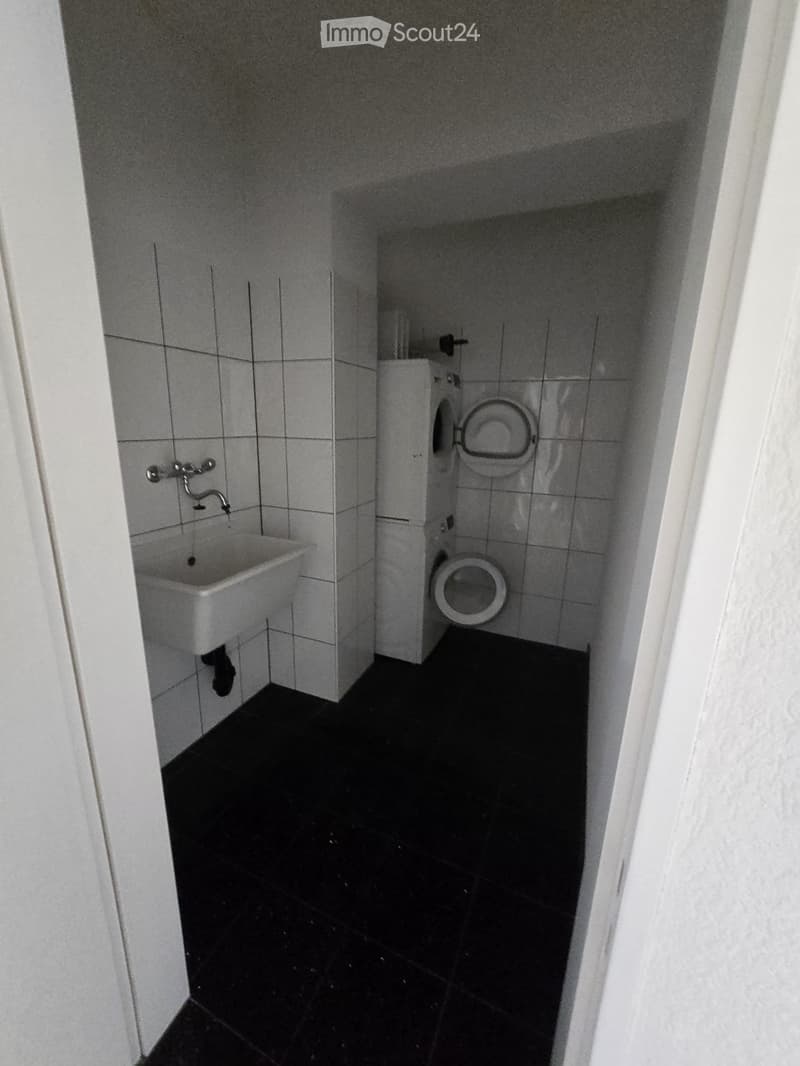 Small bathroom with a white sink and toilet, tiled walls, and dark tiled floor.