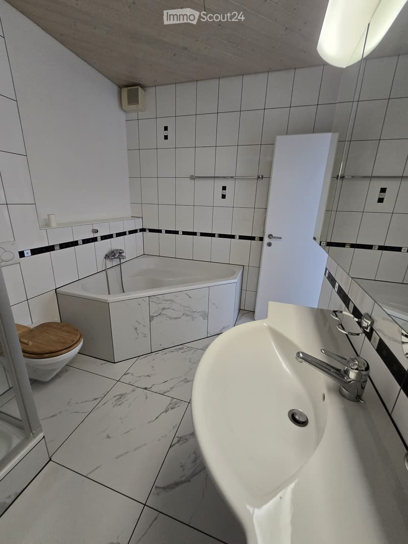 Modern bathroom with white marble tiles, a white sink with chrome faucet, a bathtub, and a toilet with a wooden seat.