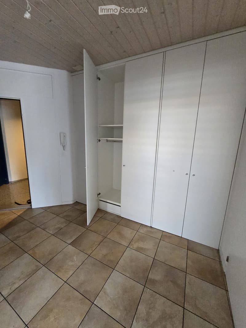 Empty room with tiled floor, white walls, and built-in white cabinets with one door open, revealing empty shelves.