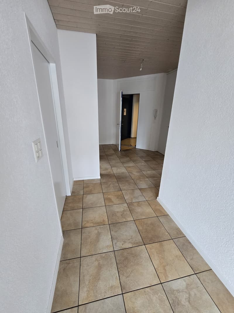 Empty hallway with tiled floor and white walls, featuring a partially open door leading to another room.
