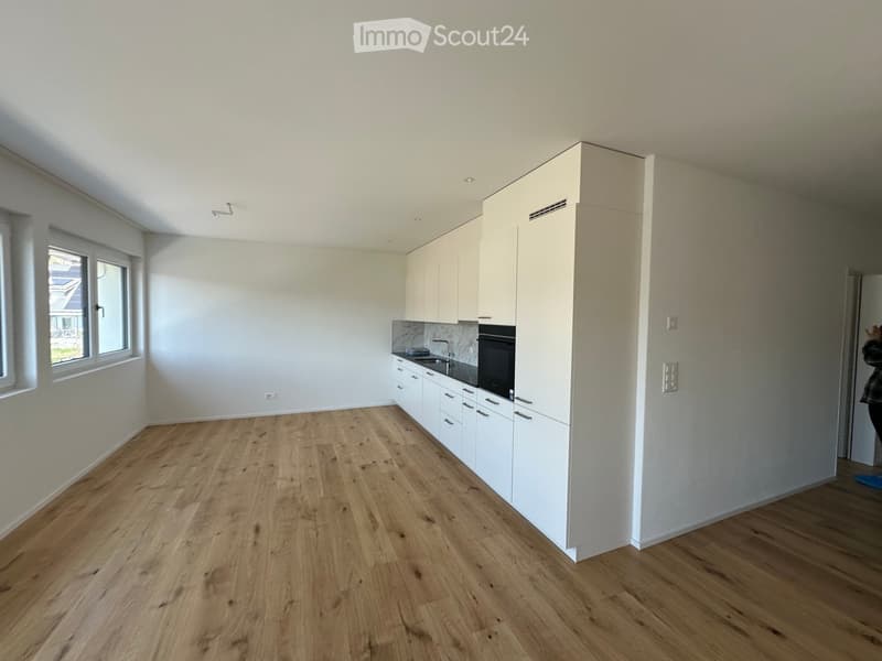 Empty kitchen with wooden floor, white cabinets, black countertops, oven, sink, faucet, windows