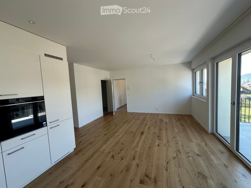 empty room, wooden floor, white walls, kitchen with oven, sliding glass doors to balcony